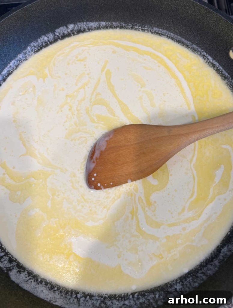 Melting butter and heavy cream in a skillet, being stirred with a wooden spoon for the sauce base.