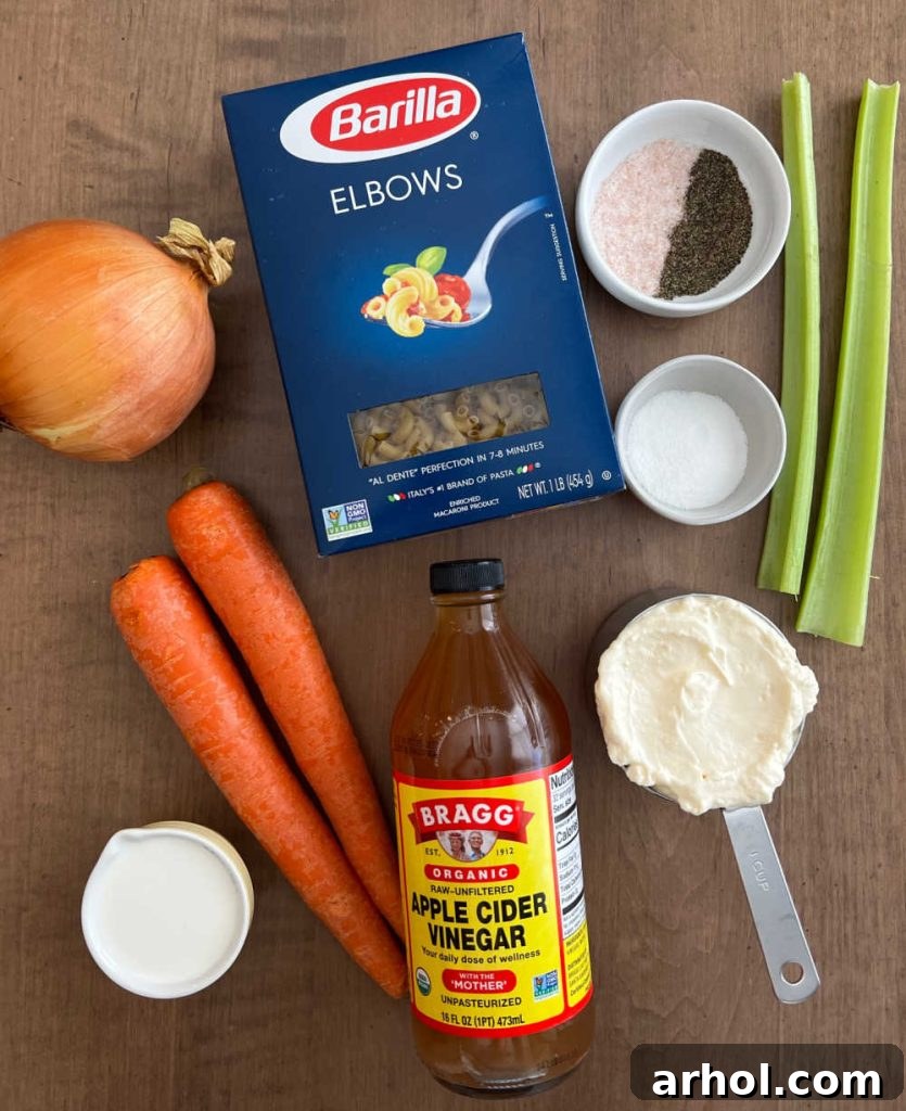 A selection of fresh ingredients laid out for Hawaiian macaroni salad preparation: elbow macaroni, yellow onion, grated carrots, finely diced celery, a jar of Best Foods mayonnaise, milk, apple cider vinegar, sugar, salt, and black pepper.