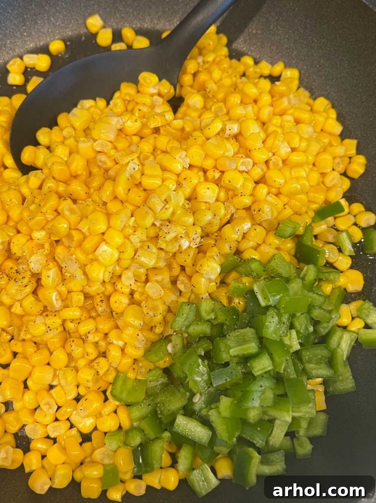 Canned corn and chopped Anaheim peppers being roasted in a large skillet over medium-high heat until slightly charred, releasing a smoky aroma.