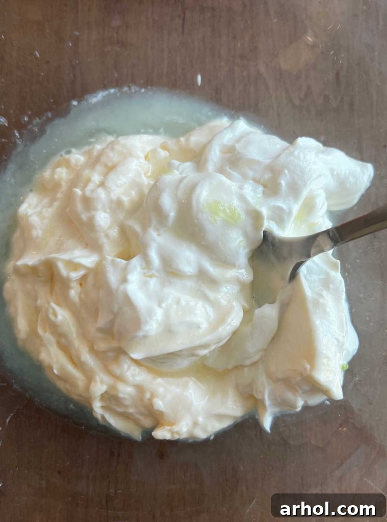 A large mixing bowl containing mayonnaise, sour cream, and fresh lime juice, being vigorously stirred together to form a smooth, creamy dressing.