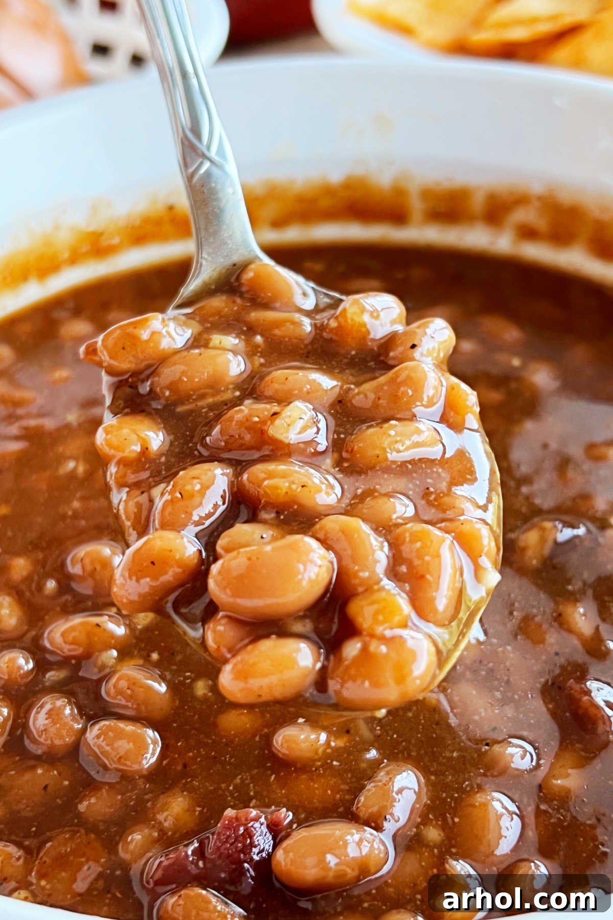 A spoonful of glistening easy brown sugar baked beans, ready to be served from a white casserole dish.