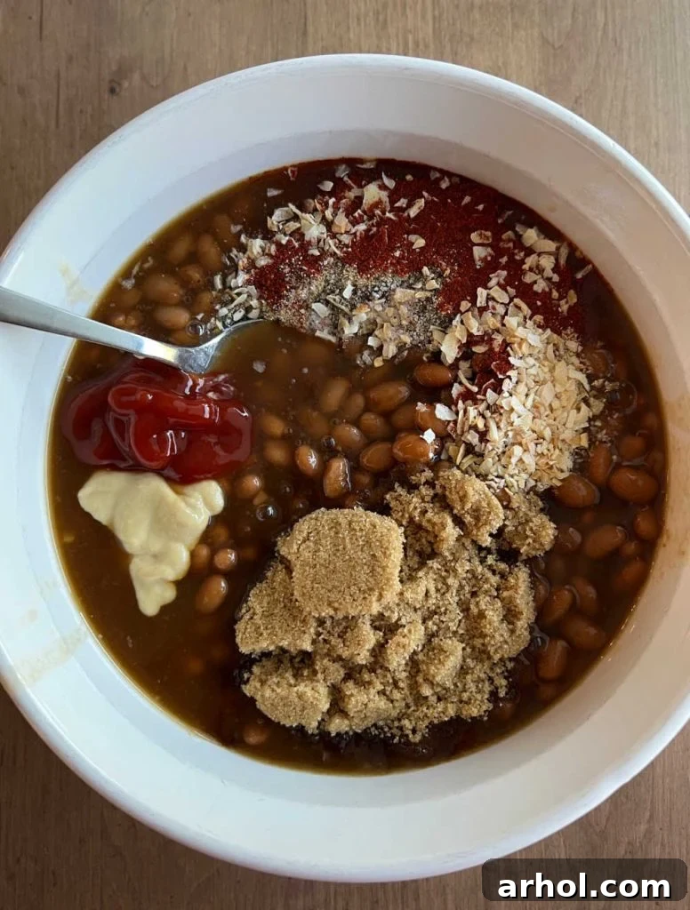 A close-up view of canned beans in a clear glass casserole dish, with brown sugar and a blend of spices sprinkled over the top, ready for mixing.