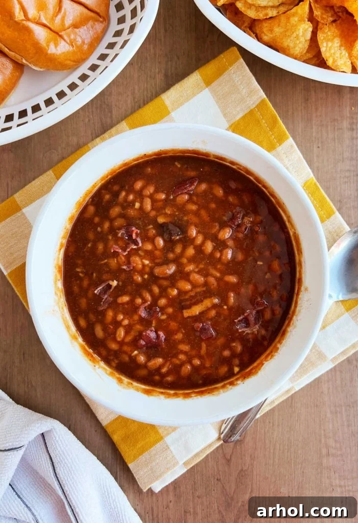 Warm, microwaved baked beans topped with crispy bacon bits, served in a white oval casserole dish on a rustic wooden table, invitingly ready to eat.