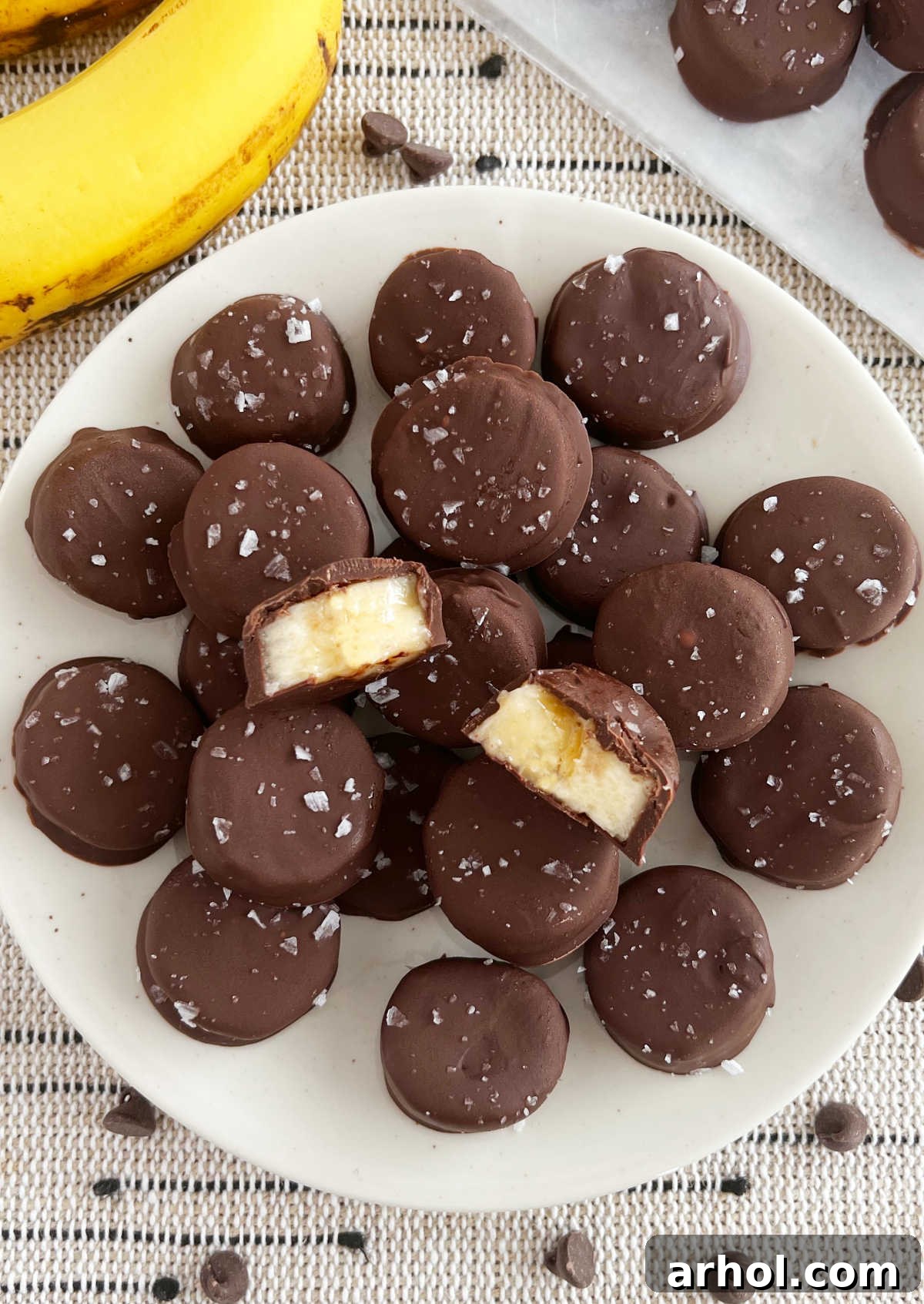 Frozen chocolate-covered banana bites with flaked salt stacked on a plate, looking inviting and delicious.