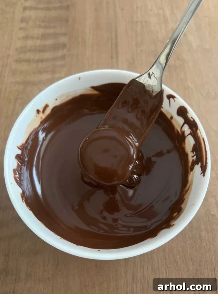 A banana slice being carefully dipped into a bowl of melted chocolate with a fork, ensuring full coverage.