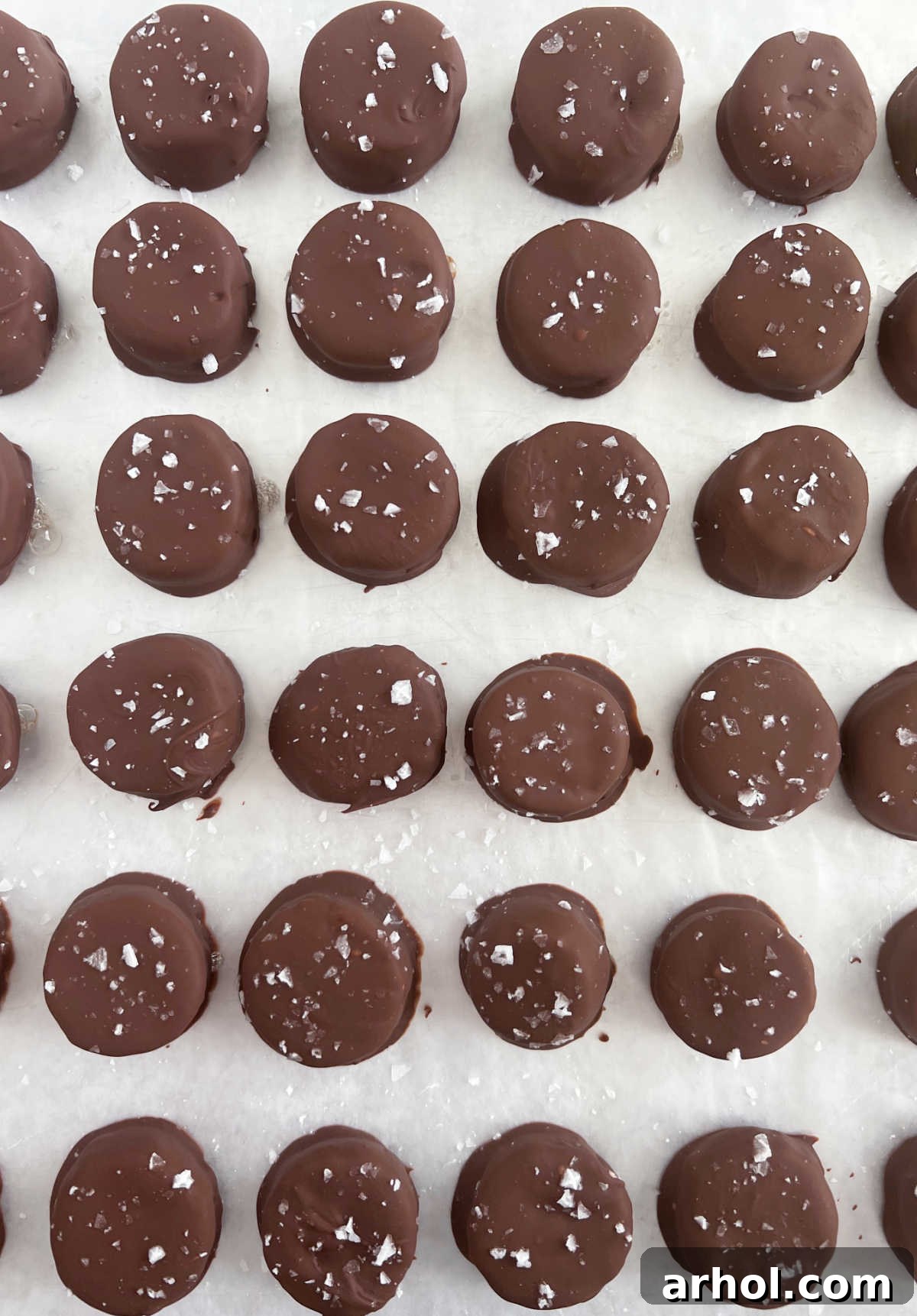 Rows of perfectly frozen chocolate banana bites, sprinkled with sea salt, neatly arranged on a parchment paper-lined baking sheet, ready for enjoyment.