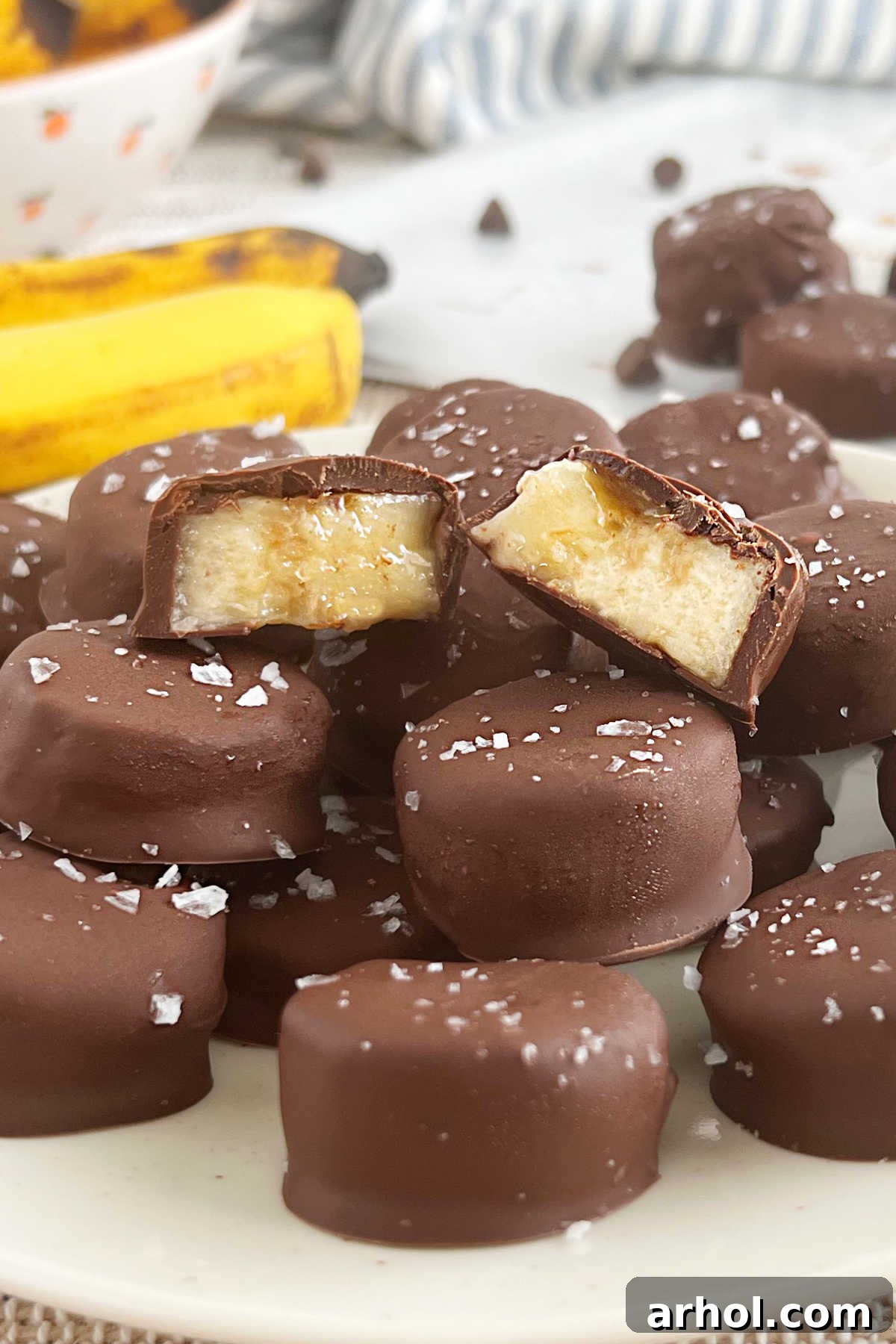 A stack of frozen chocolate banana bites, cut open to reveal the creamy banana interior, neatly arranged on a plate.