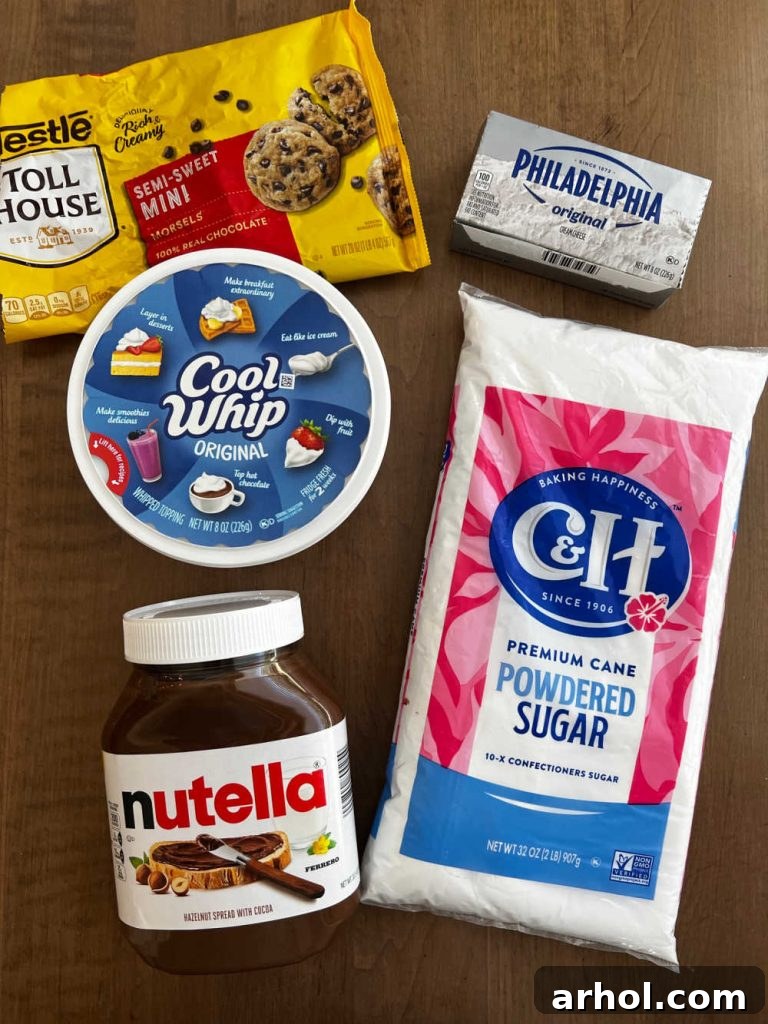 All essential ingredients for the Nutella cheesecake dip laid out neatly: a jar of Nutella, a tub of Cool Whip, a block of cream cheese, a bowl of powdered sugar, and a small dish of mini chocolate chips, highlighting the simplicity of the recipe.