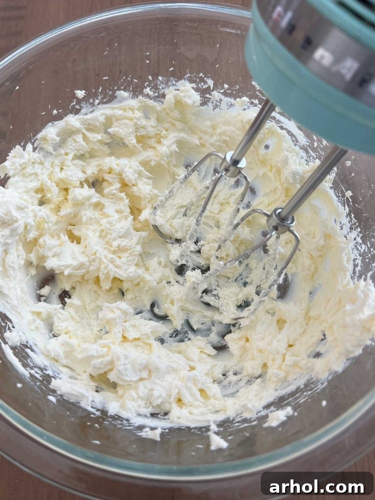 Beating softened cream cheese in a large mixing bowl with an electric hand mixer until it reaches a smooth and creamy consistency, the essential first step for this no-bake dip.