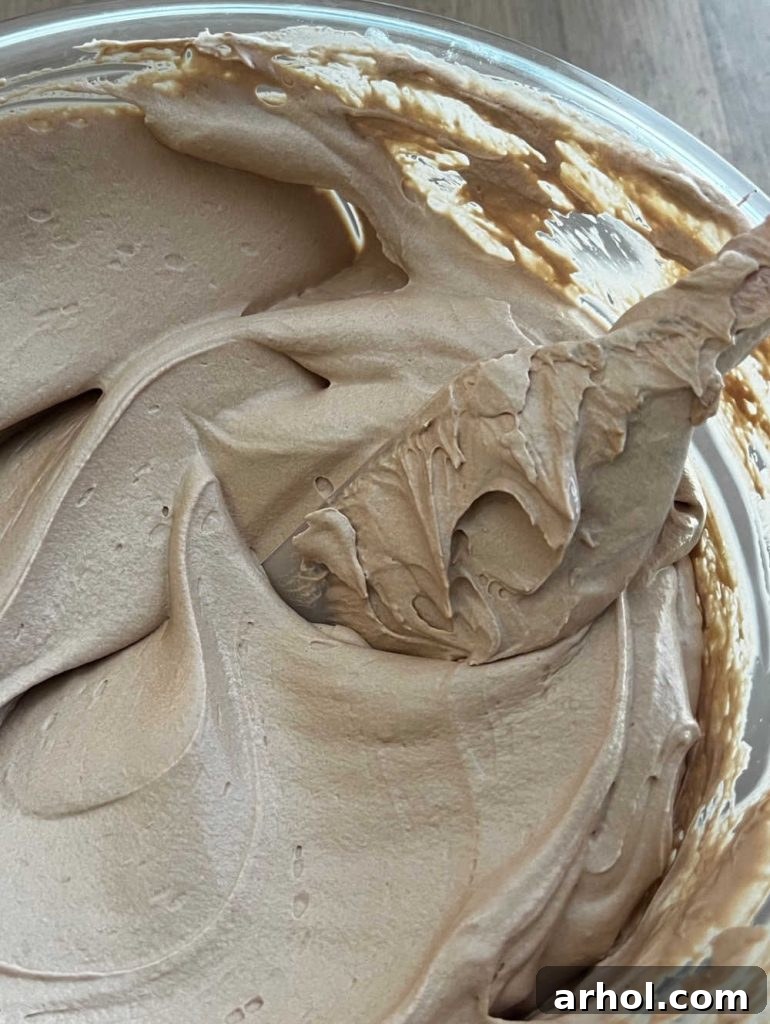 A rubber spatula carefully folding thawed Cool Whip into the Nutella cream cheese mixture in a mixing bowl, illustrating the technique to ensure a light and fluffy consistency for the finished dip.