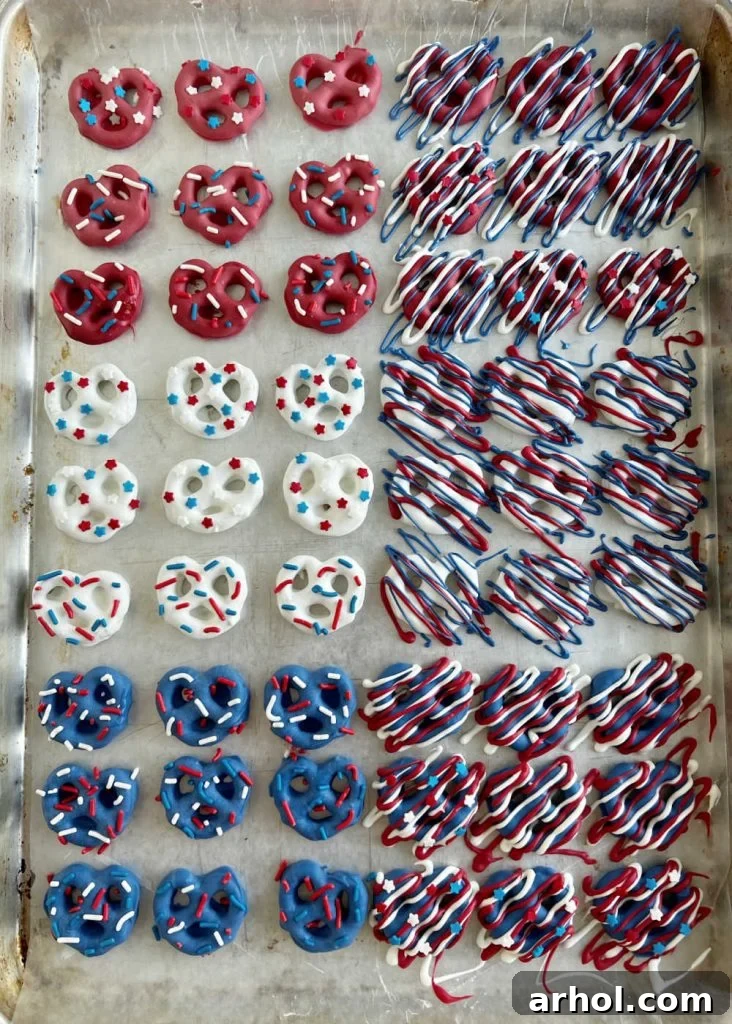 Decorated red, white, and blue patriotic pretzels on a wax paper-lined baking sheet, showcasing festive colors and patterns.
