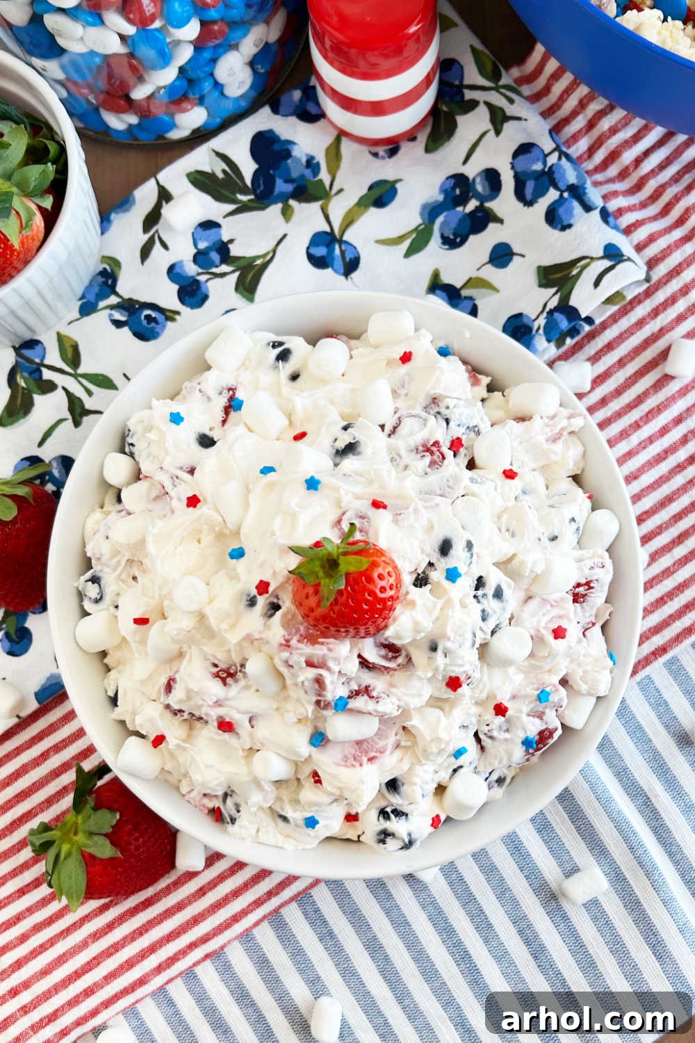 A large bowl of Red White and Blue Cheesecake Salad, brimming with fresh berries and mini marshmallows, set on a patriotic outdoor table for the Fourth of July.