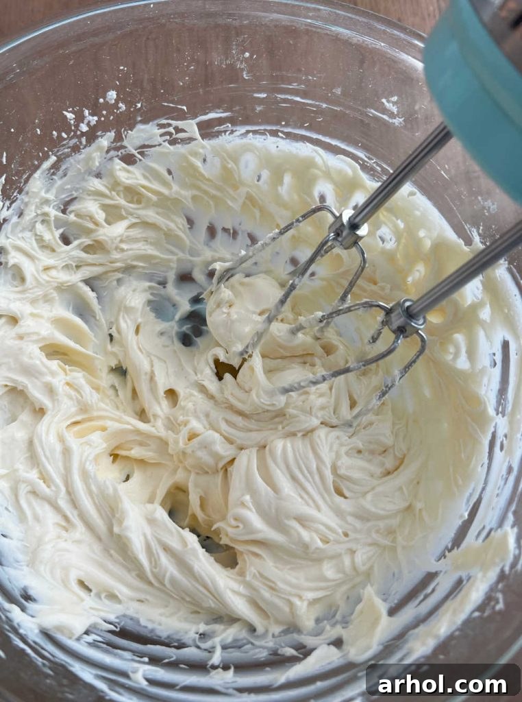 Mixing cream cheese and powdered sugar with an electric mixer in a bowl for the cheesecake salad dressing.