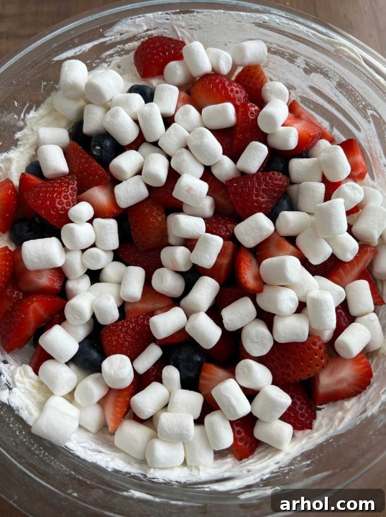 Fresh berries and mini marshmallows being folded into the creamy cream cheese mixture.