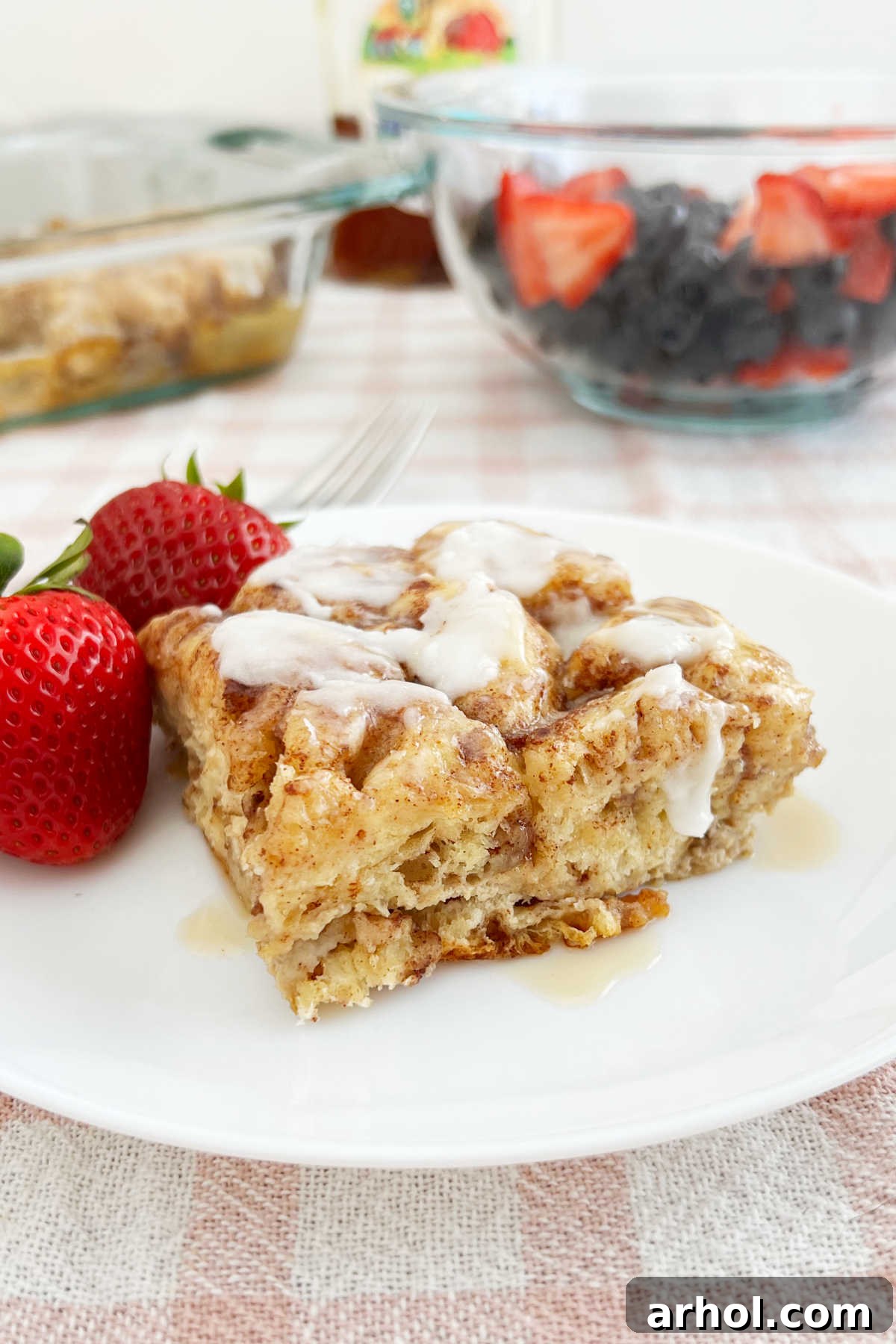cinnamon roll casserole with frosting, strawberries and maple syrup on the table
