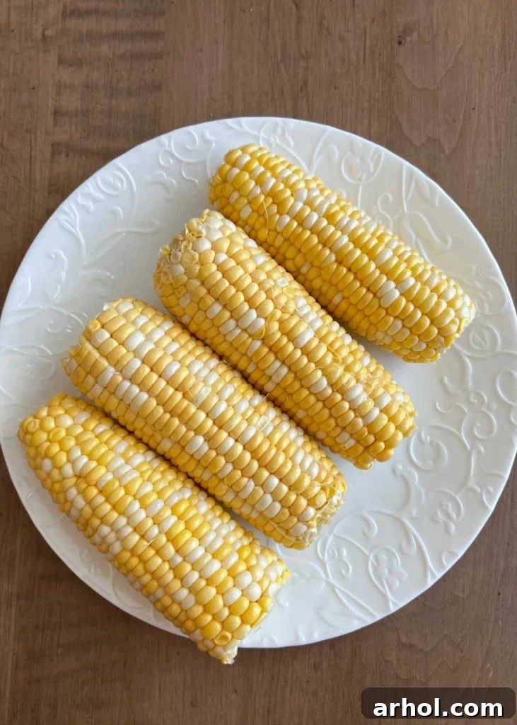 Four ears of perfectly shucked corn on the cob without husks, arranged on a plate.