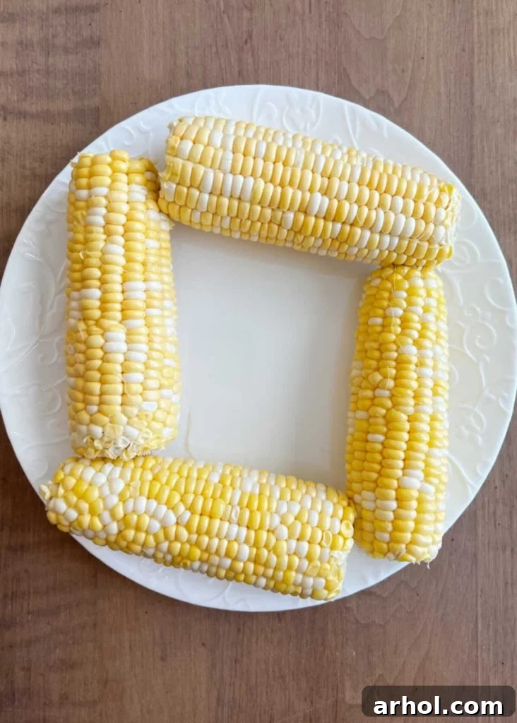 Husked corn on the cob arranged in a single layer on a microwave-safe plate.