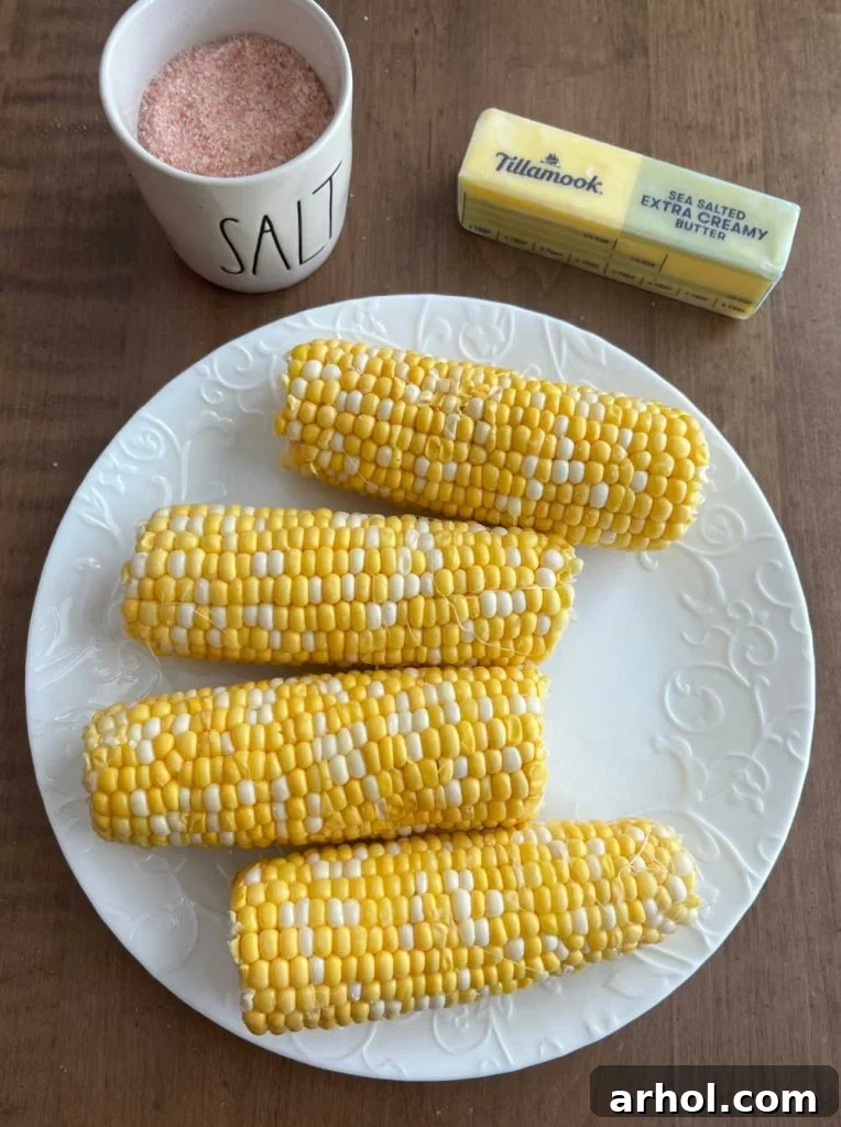 Four ears of fresh corn on the cob, a stick of butter, and a sprinkle of sea salt, ready for preparation.