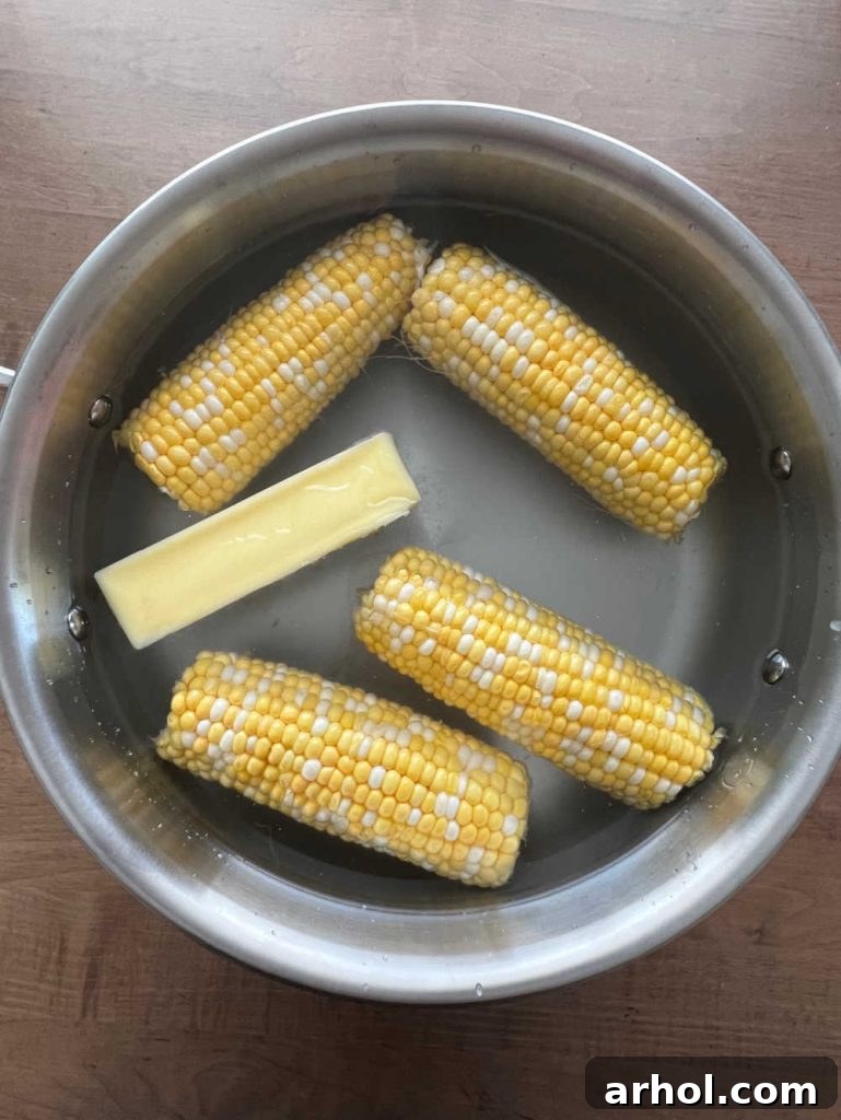 Corn on the cob ears submerging into a pot of boiling water with a stick of butter melting, creating a savory butter bath.