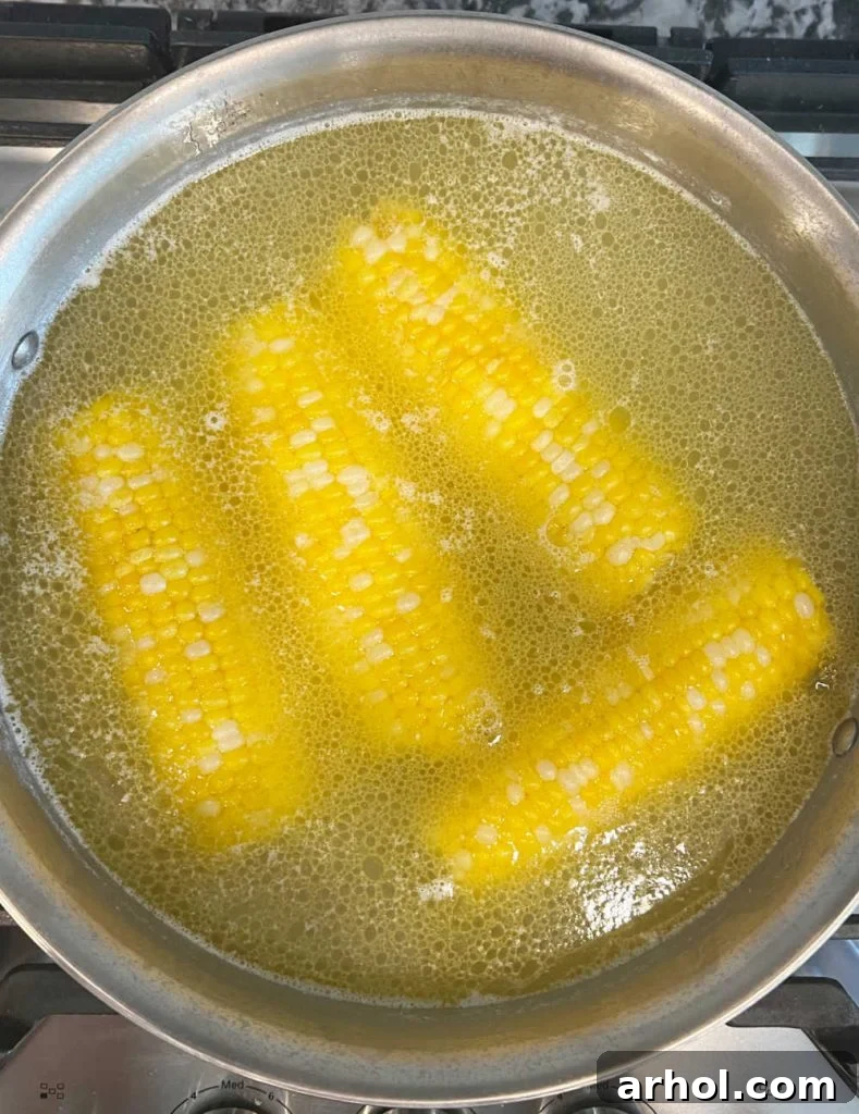 Several ears of corn on the cob simmering in a pot of water on the stove, appearing bright yellow and perfectly cooked.