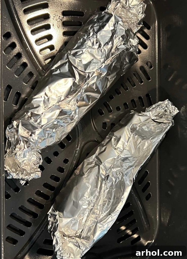 corn on the cob in foil in air fryer basket.