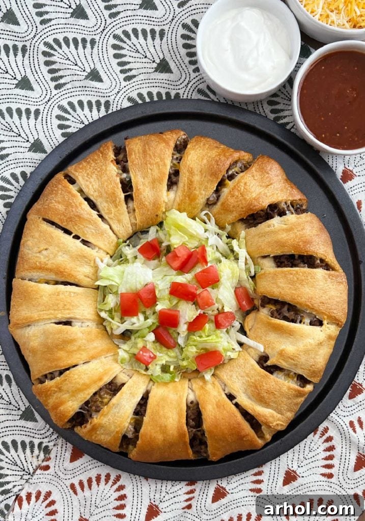 Golden baked taco ring with crescent roll dough and ground beef, served on a platter with fresh lettuce and tomatoes in the center, ready for sharing.
