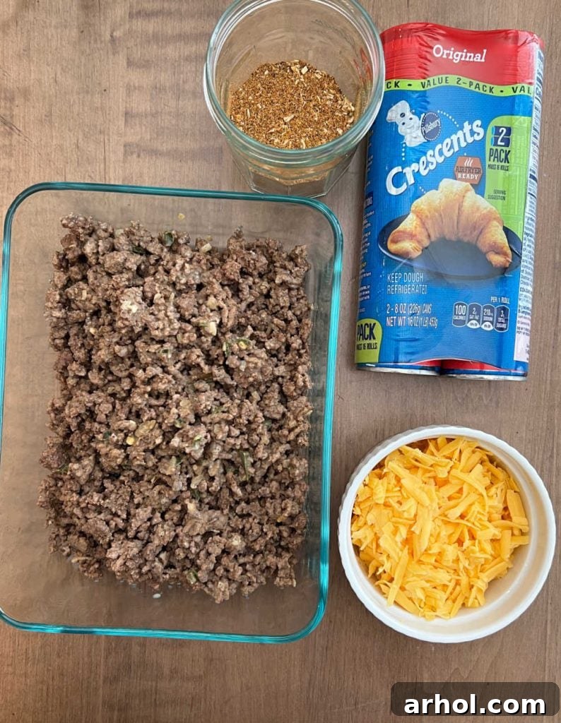 Raw ingredients for taco ring including ground beef, taco seasoning packet, two cans of crescent roll dough, and a bowl of shredded cheese.