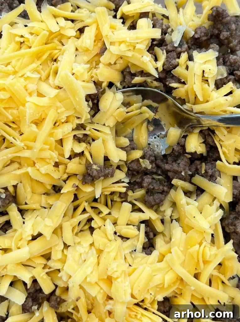 Close-up of seasoned ground beef with melted shredded cheese being stirred in a skillet, creating a cohesive taco filling.