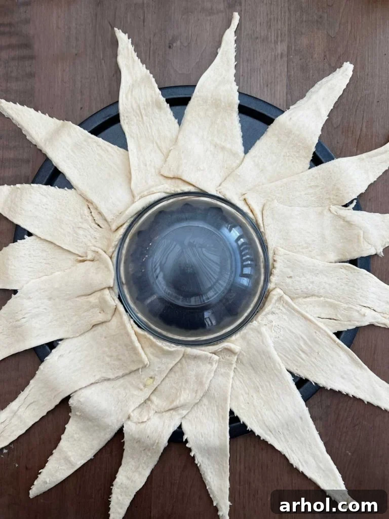 Crescent roll dough triangles arranged in a circular pattern on a pizza pan around a small glass bowl, forming the base of the taco ring.