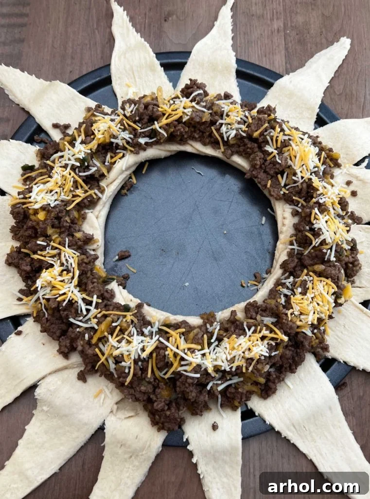 Cooked taco meat and shredded cheese layered on the wide ends of crescent roll dough triangles, ready to be folded.