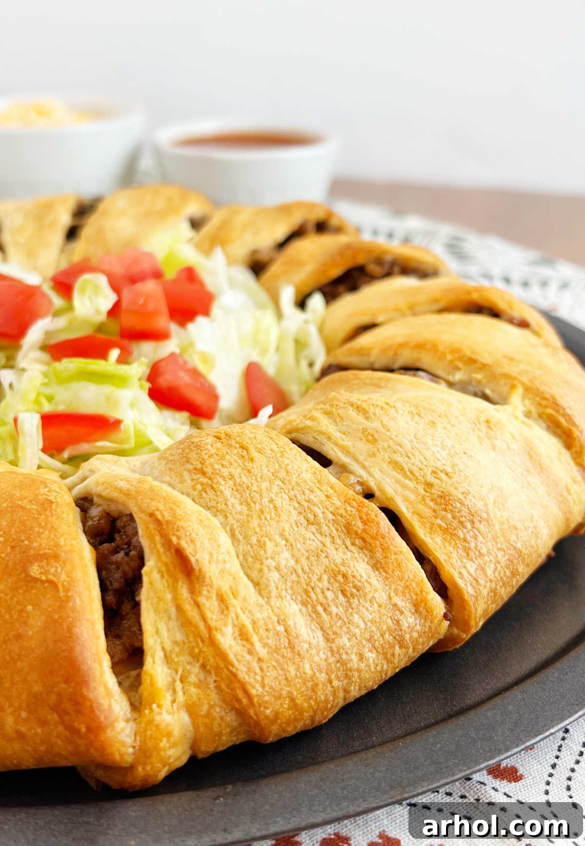 Side view of a freshly baked taco ring with a hollow center filled with crisp lettuce and diced tomatoes, ready for serving.