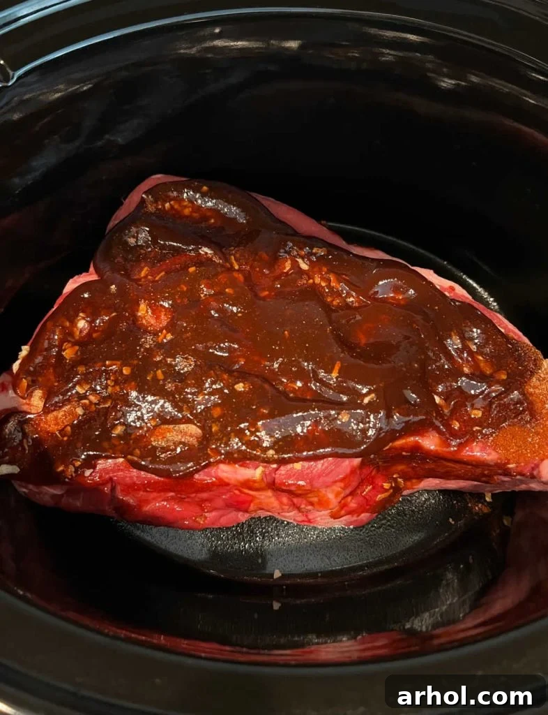 beef roast in slow cooker with bbq sauce on top.