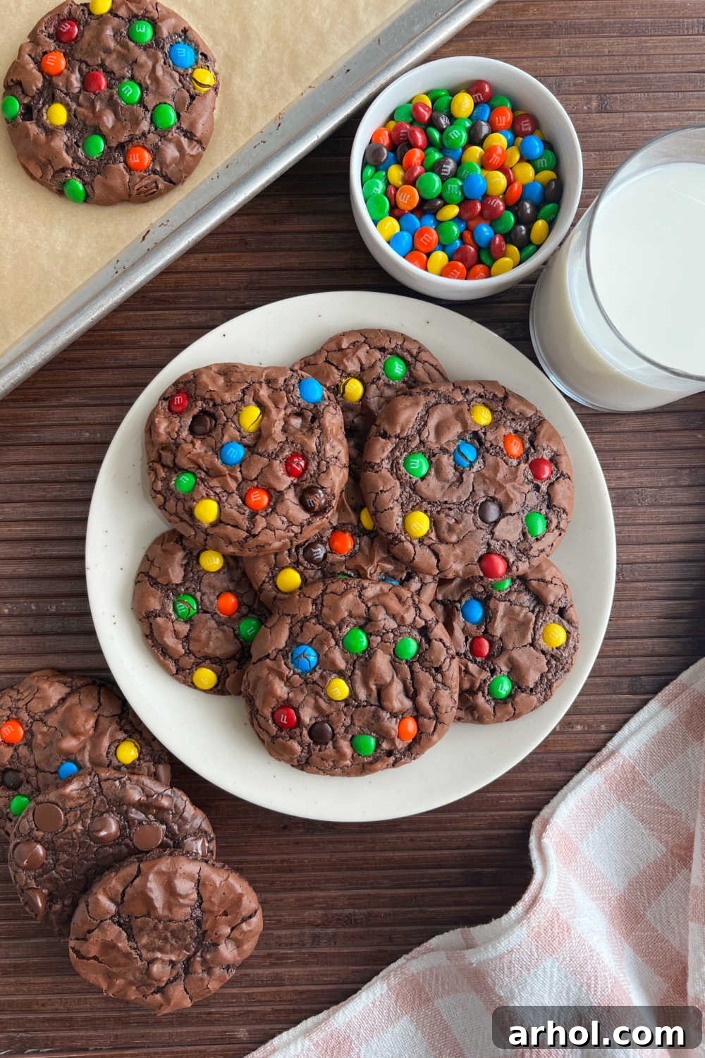 Fudgy brownie mix cookies, garnished with colorful mini M&M candies, neatly arranged on a plate beside a tall glass of fresh milk, inviting a delightful snack.