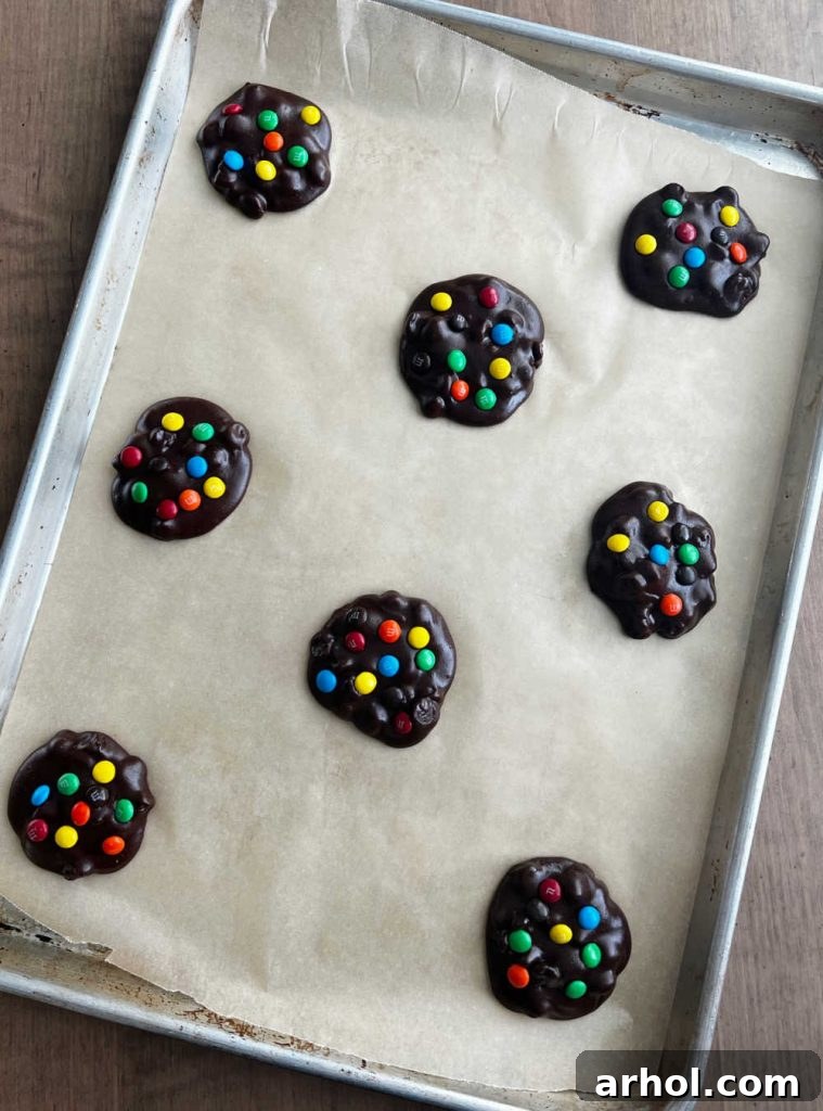 Unbaked brownie batter cookies, generously topped with vibrant mini M&M candies, neatly spaced on a prepared baking sheet, ready for the oven.