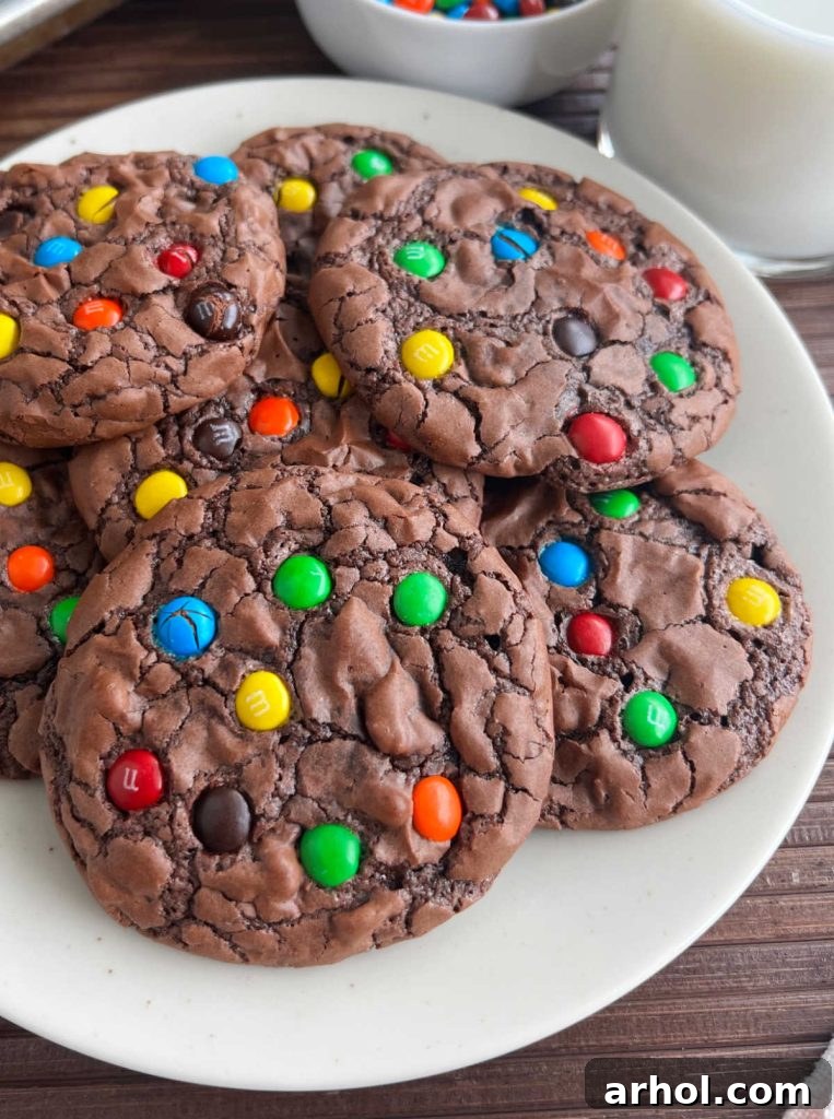 A delightful close-up of fudgy brownie cookies adorned with colorful M&M minis, stacked invitingly on a white plate, ready to be enjoyed.