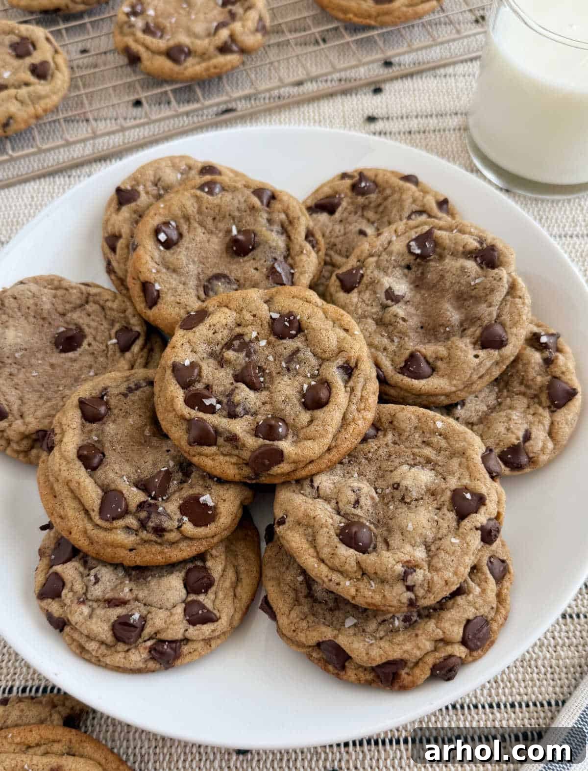 Freshly baked chewy chocolate chip cookies with flaky sea salt on a plate, served with a glass of milk.