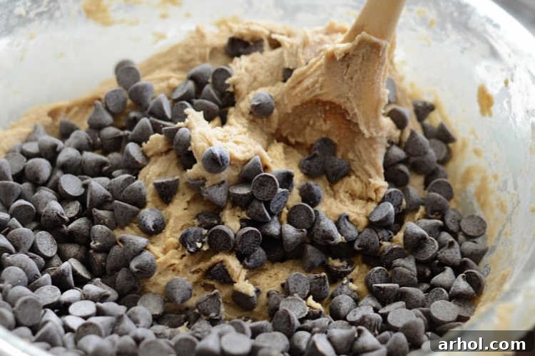 Folding semi-sweet chocolate morsels into cookie dough in a mixing bowl.