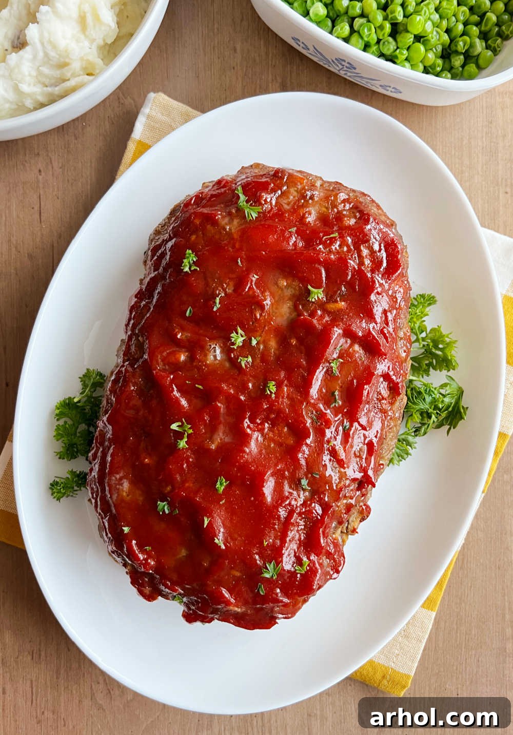 meatloaf with stuffing on a platter with parsley, mashed potatoes and peas.