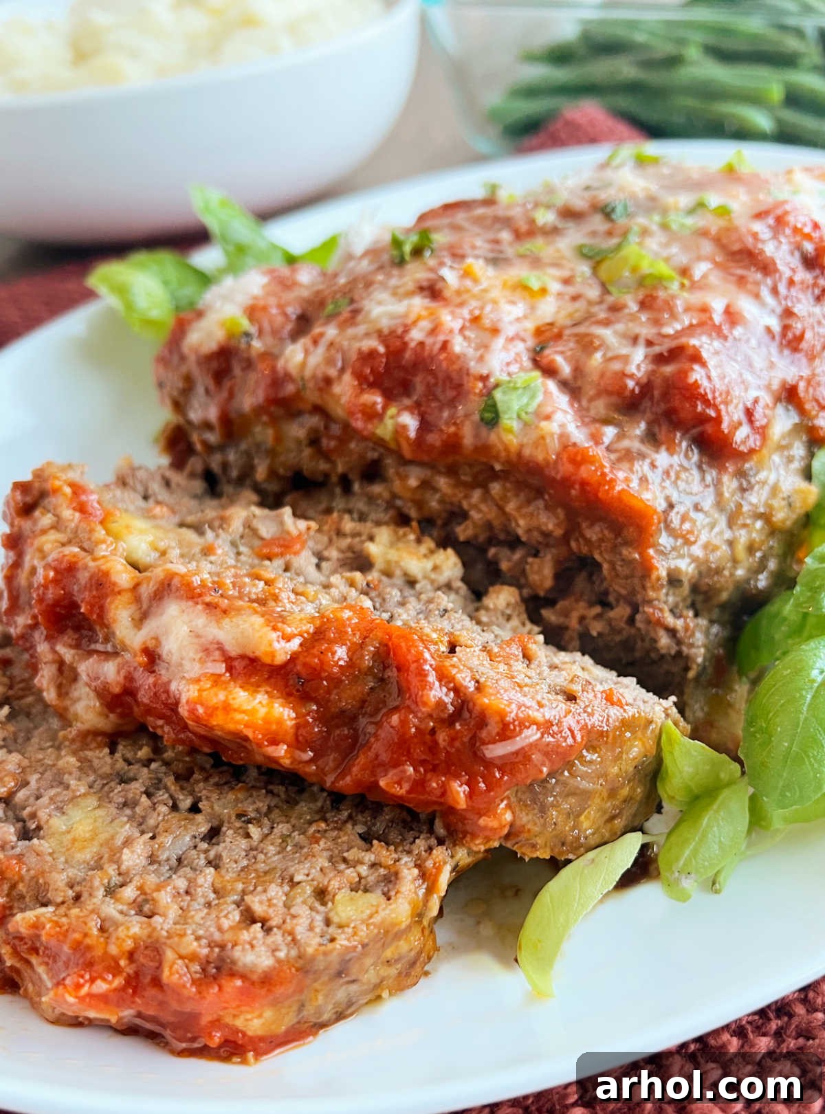 Italian meatloaf with marinara and Parmesan cheese on platter with basil.