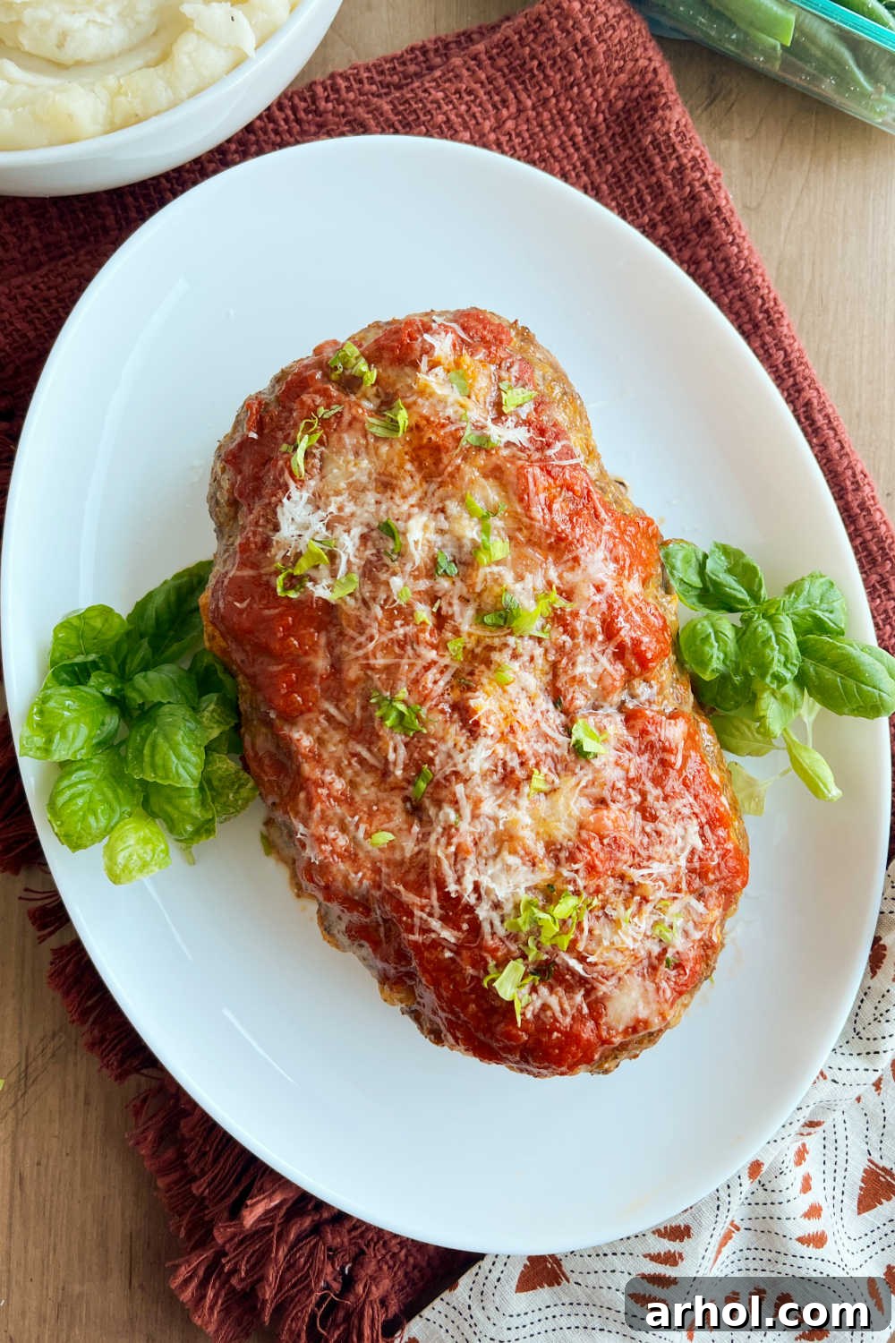 Italian meatloaf on platter with mashed potatoes and green beans.