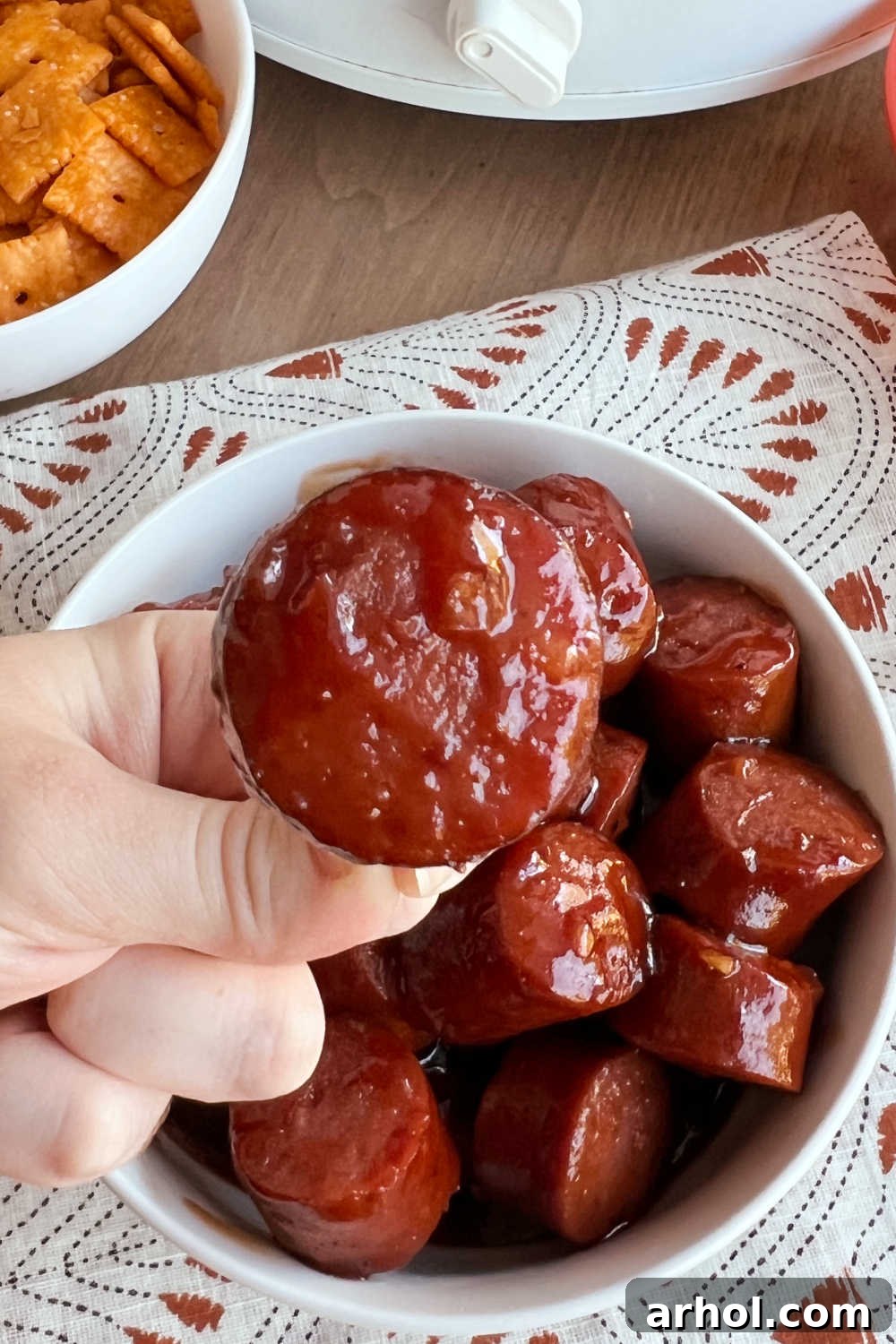 A hand holding a toothpick with a brown sugar BBQ kielbasa bite, showcasing the appetizing glaze and perfect size for snacking.