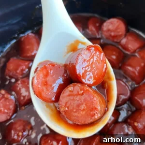 Slow cooker kielbasa bites with BBQ sauce, presented in a serving spoon over a crockpot, highlighting the glossy glaze.