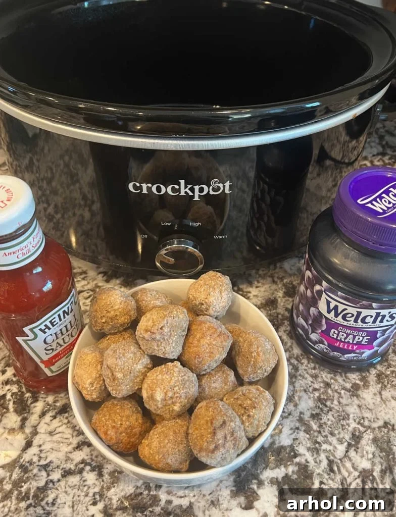 slow cooker with bottle of Heinz chili sauce, frozen meatballs and jar of grape jelly.