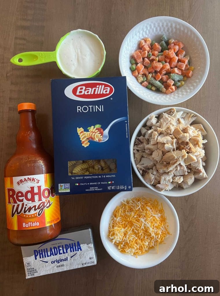 Individual ingredients for Buffalo Chicken Casserole including cooked chicken, buffalo sauce, ranch dressing, rotini pasta, cream cheese, frozen veggies, and shredded cheese.