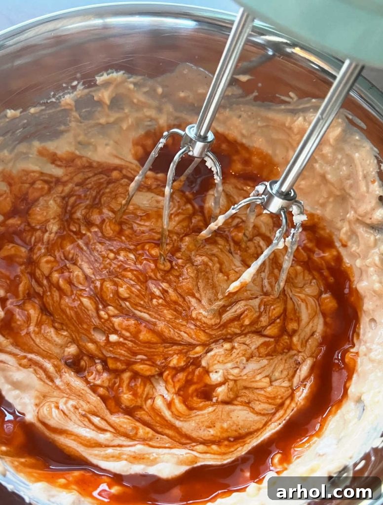 Mixing cream cheese, ranch dressing, and buffalo wing sauce in a large mixing bowl to create the creamy sauce base for the casserole.