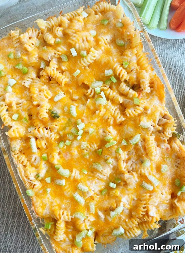 Freshly baked Buffalo Chicken Casserole, bubbly with melted golden cheese, garnished with chopped celery on a dining table.