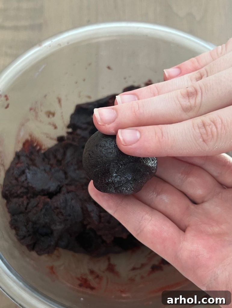 Hands forming a perfectly round cake ball, demonstrating the shaping process for Halloween cake pops.