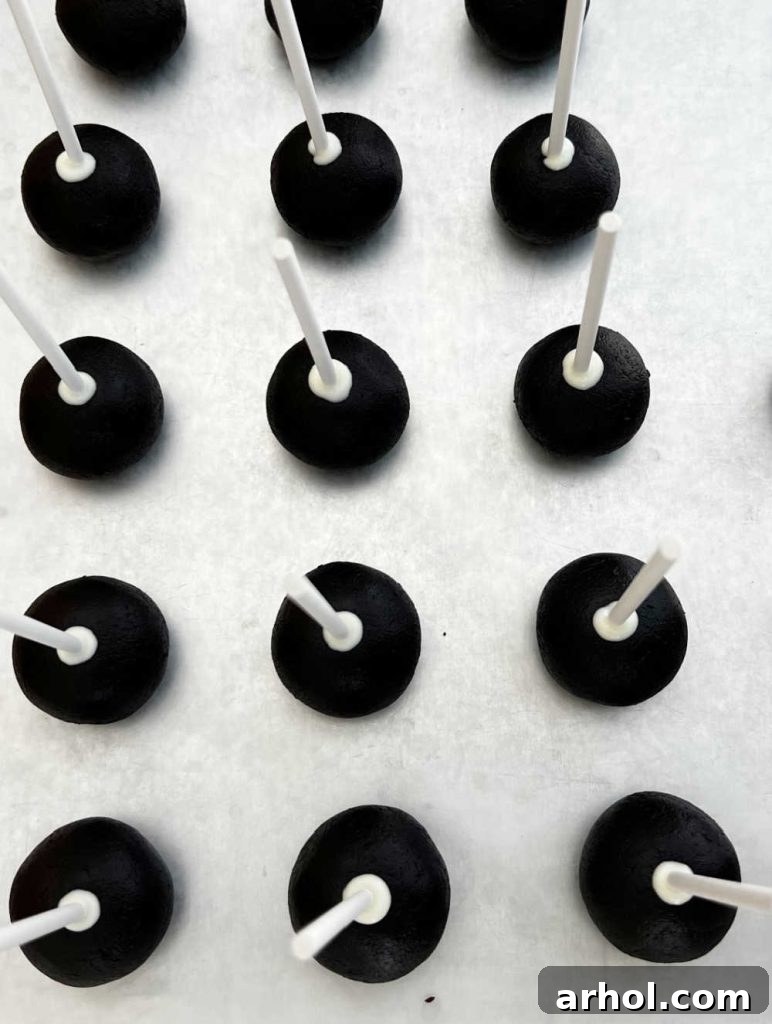 Chilled chocolate cake balls, each neatly placed on a cake pop stick, arranged on a baking tray ready for decorating.