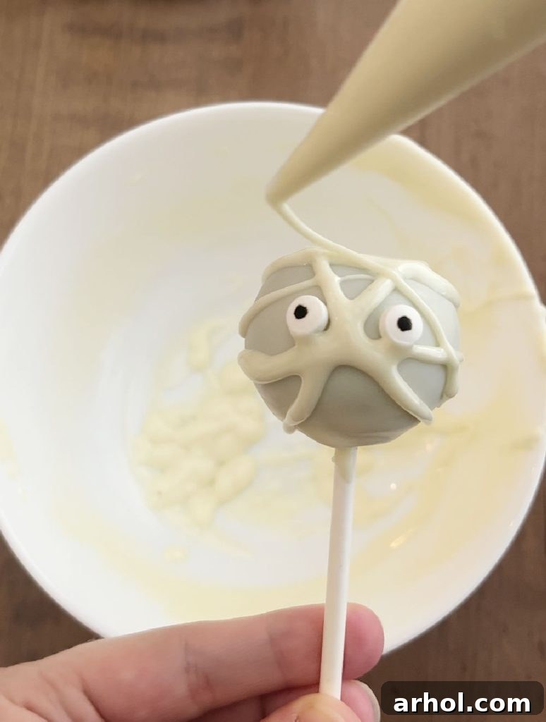 A step-by-step guide to decorating a mummy cake pop, showing white candy melt dipping, candy eye placement, and drizzling for bandages.