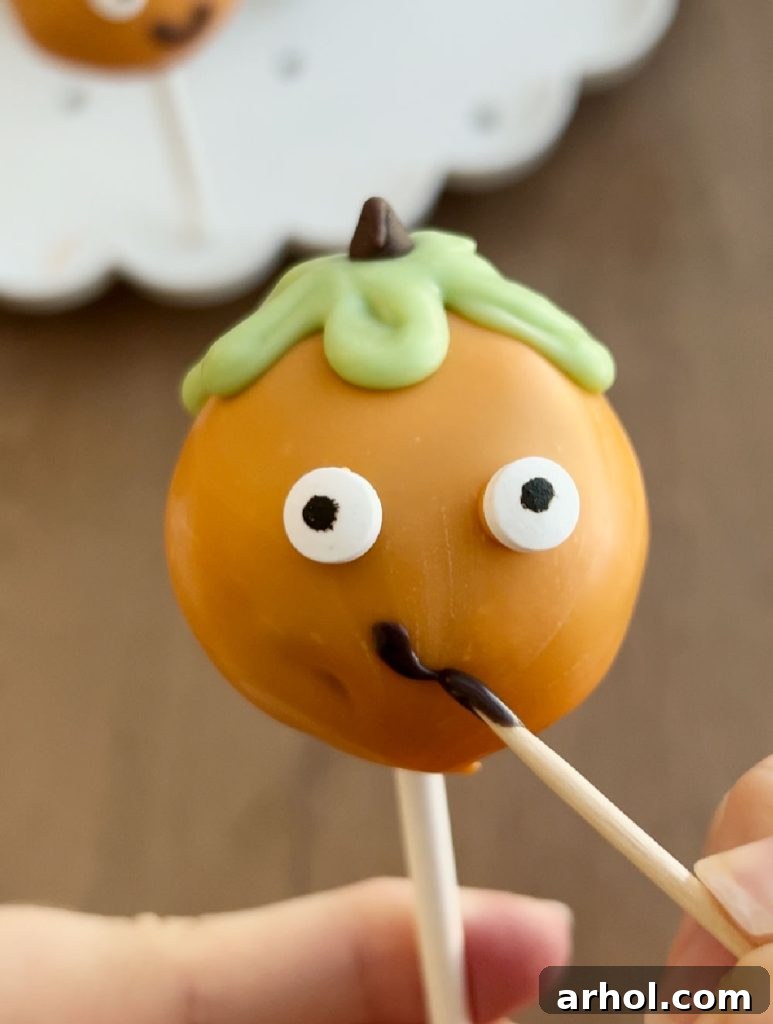 Detailed process of decorating a pumpkin cake pop, featuring orange candy melt coating, candy eyes, green vines, and a mini chocolate chip stem.